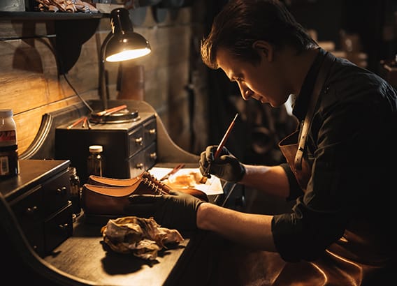 Picture of young concentrated man shoemaker at footwear workshop.