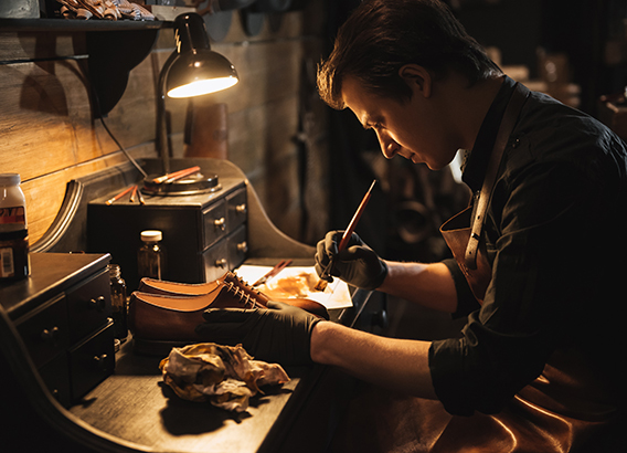 Picture of young concentrated man shoemaker at footwear workshop.