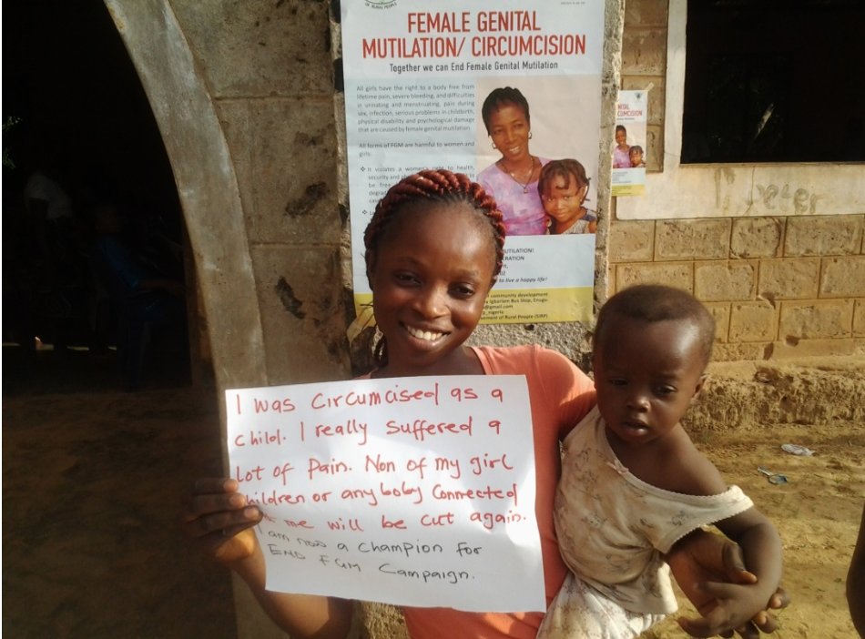 A woman holds a sign saying that she will never allow any of her children to be mutilated like she was.