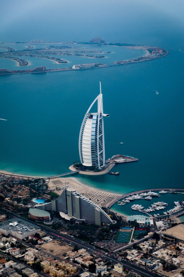 In the Photo: the Palms in the background of Dubai, UAE. Photo Credit: Christoph Schulz via Unsplash.