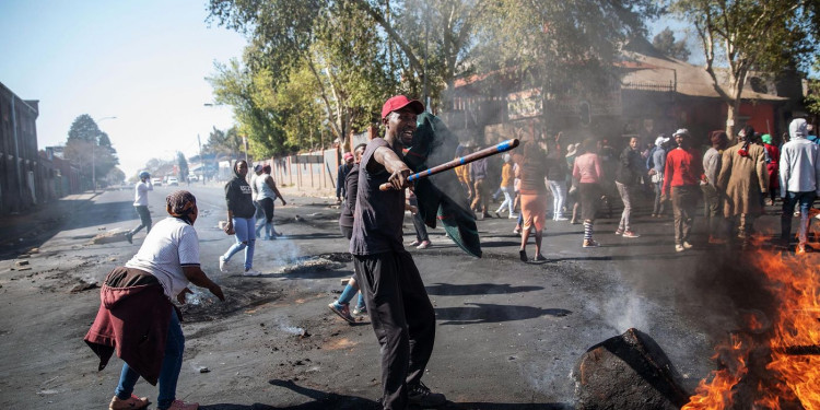 A man holds a stick in front of burning furniture in the streets during riots in Johannesburg, SA.  
Credit: Getty Images