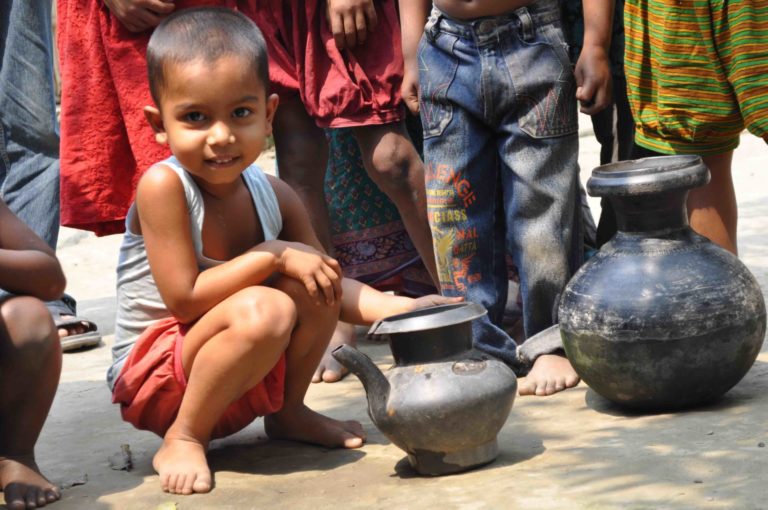 A young boy in Bangladesh plays next to his mother's water vessels.