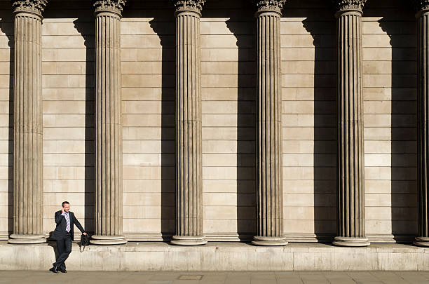 "London, United Kingdom - March 28, 2012: City worker talking on a mobile phone outside the imposing facade of the Bank of England during the morning rush hour. The Bank of England is situated on Threadneedle Street in the capitals traditional financial district, the City of London."