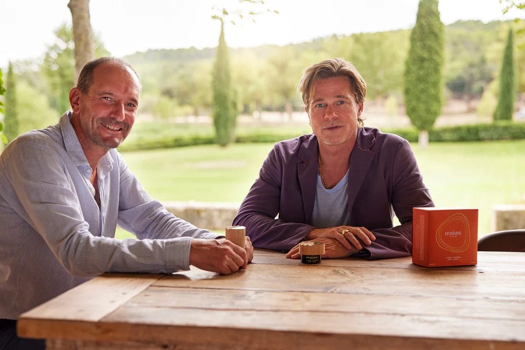[Image description: Brad Pitt sitting at a table in a green field.] Via le-domaine-skincare.myshopify.com]