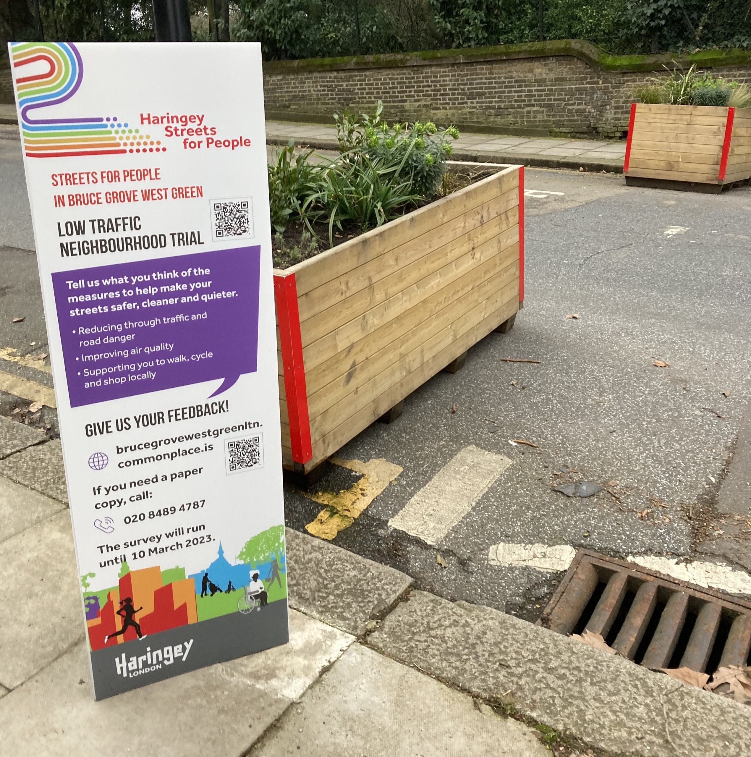 A sign requesting survey responses about the Low Traffic Neighbourhood trial, alongside the scheme's barriers