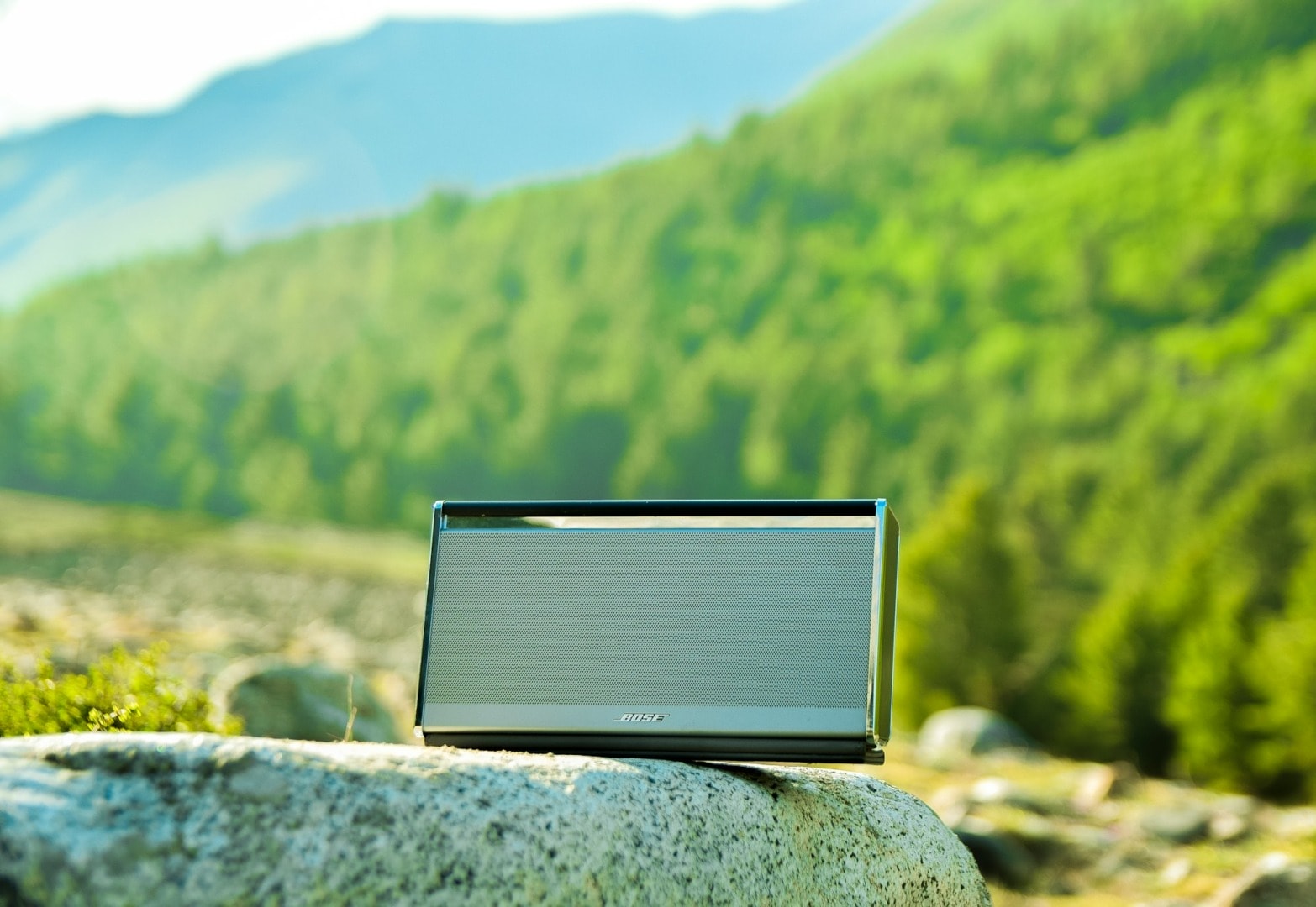 A portable speaker sitting on a rock, under sunlight.