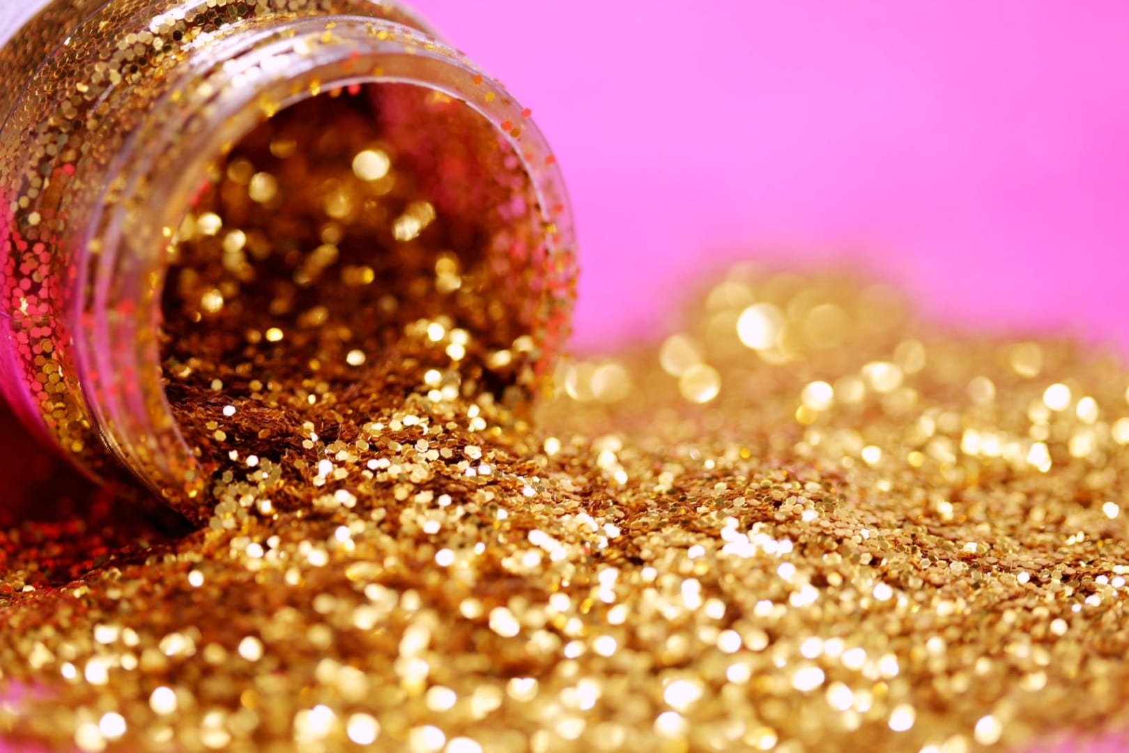 gold glitter spilled from a bottle into a pink background.