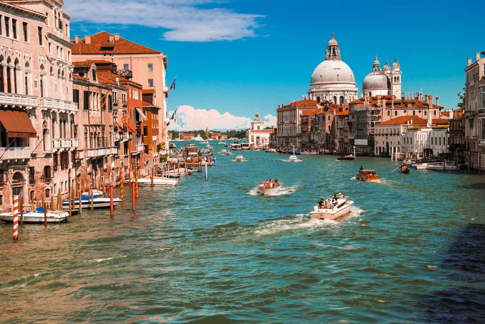 Boats pass through the Venice Grand Canal on a bright, sunny day. 