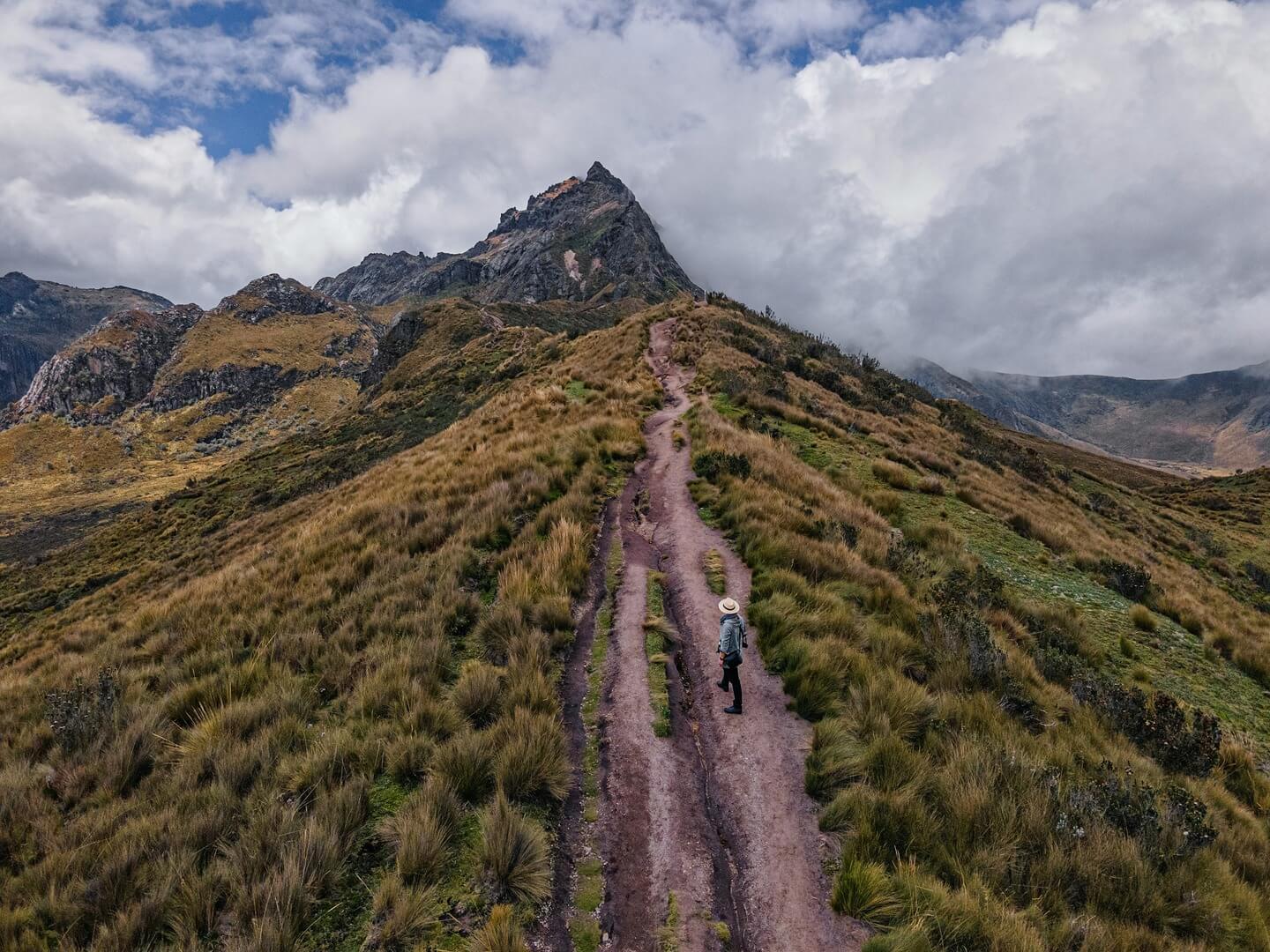 A man stands on a trail that follows the ridge of a mountain.
