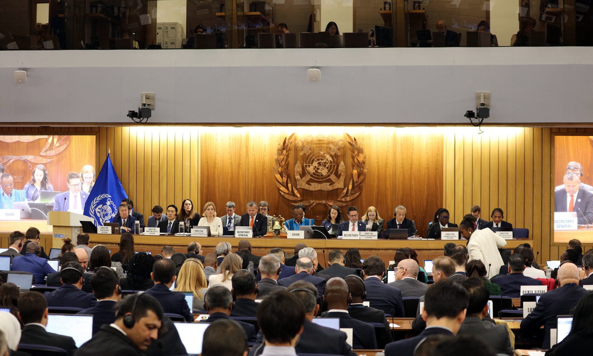A group of people, many with headphones, attend a meeting.