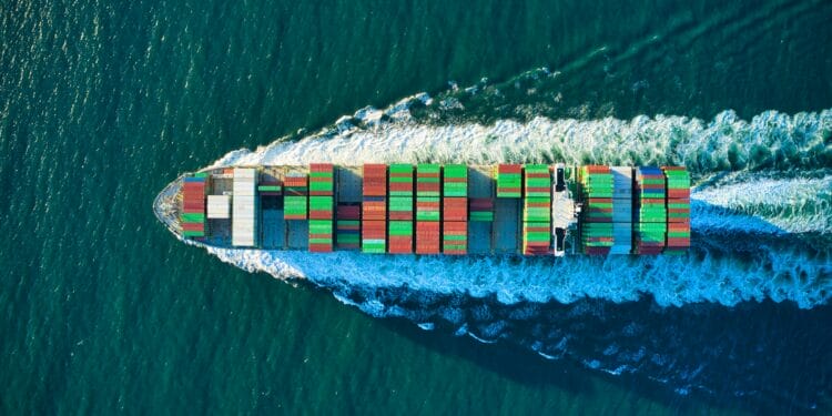A cargo ship covered with containers leaves a wake as it passes over the surface of the ocean.