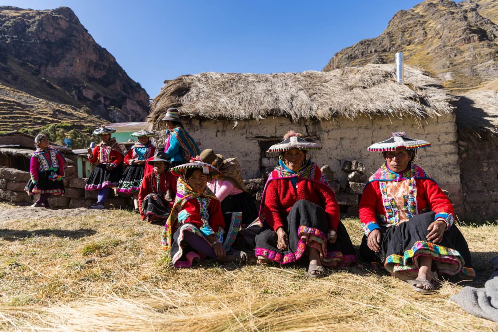 A group of women sit in front of a rural Andean home. 