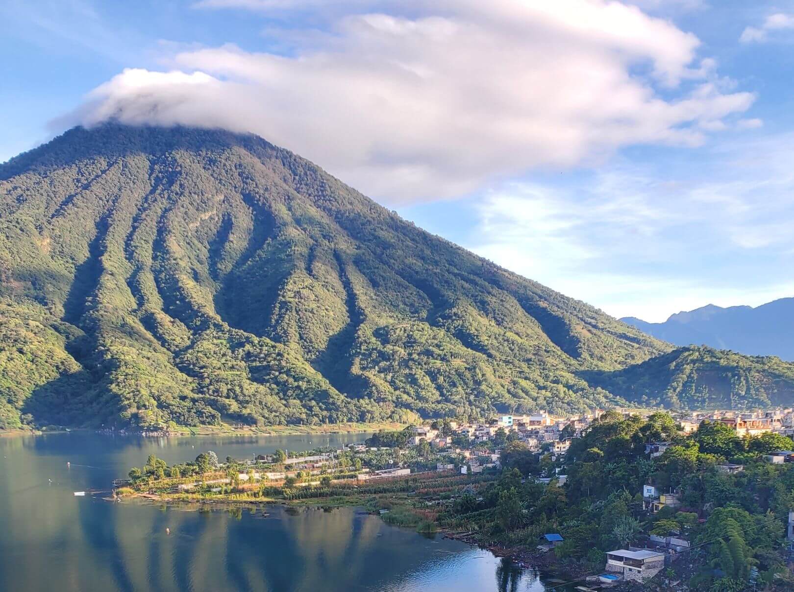 A section of lake alongside a town with a volcano in the background.