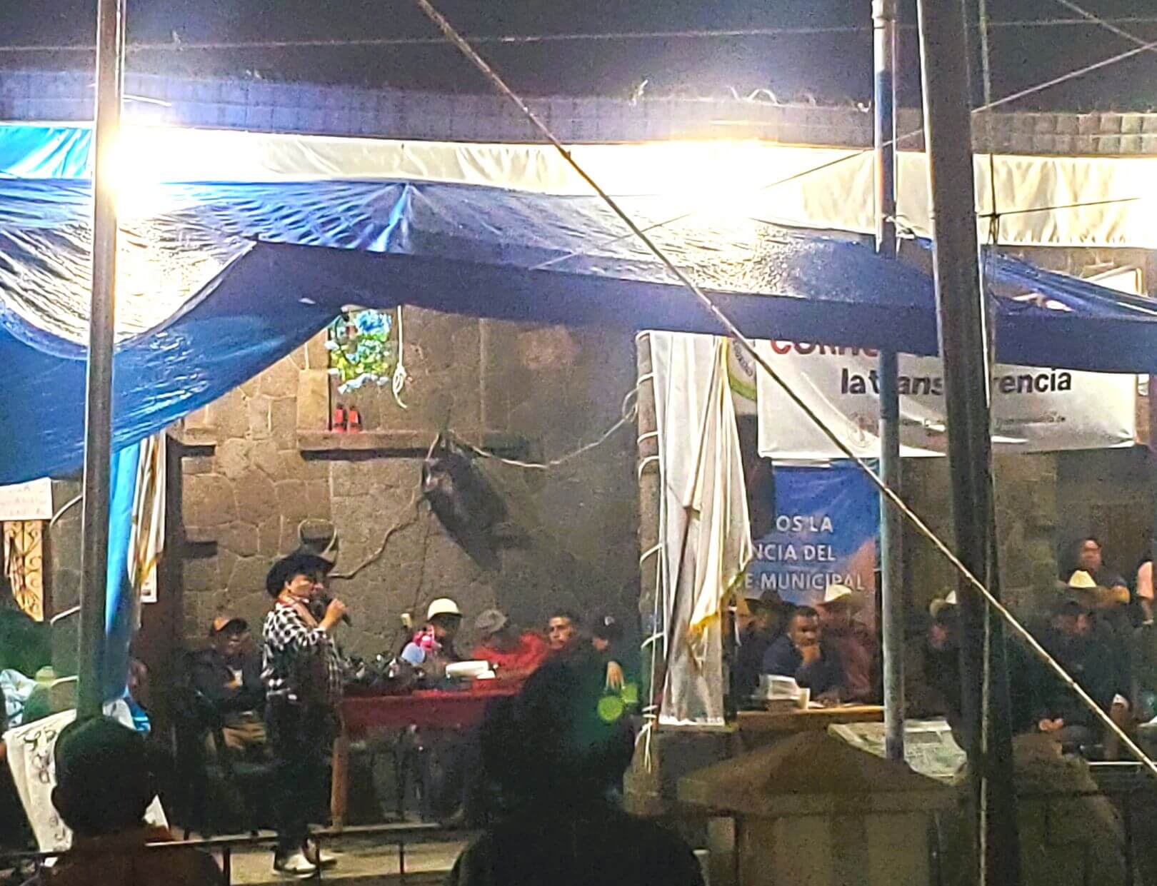 A man speaks into a microphone in front of an illuminated building.