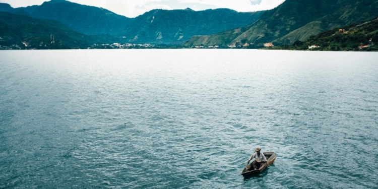 A fisherman paddles a canoe on a massive lake.