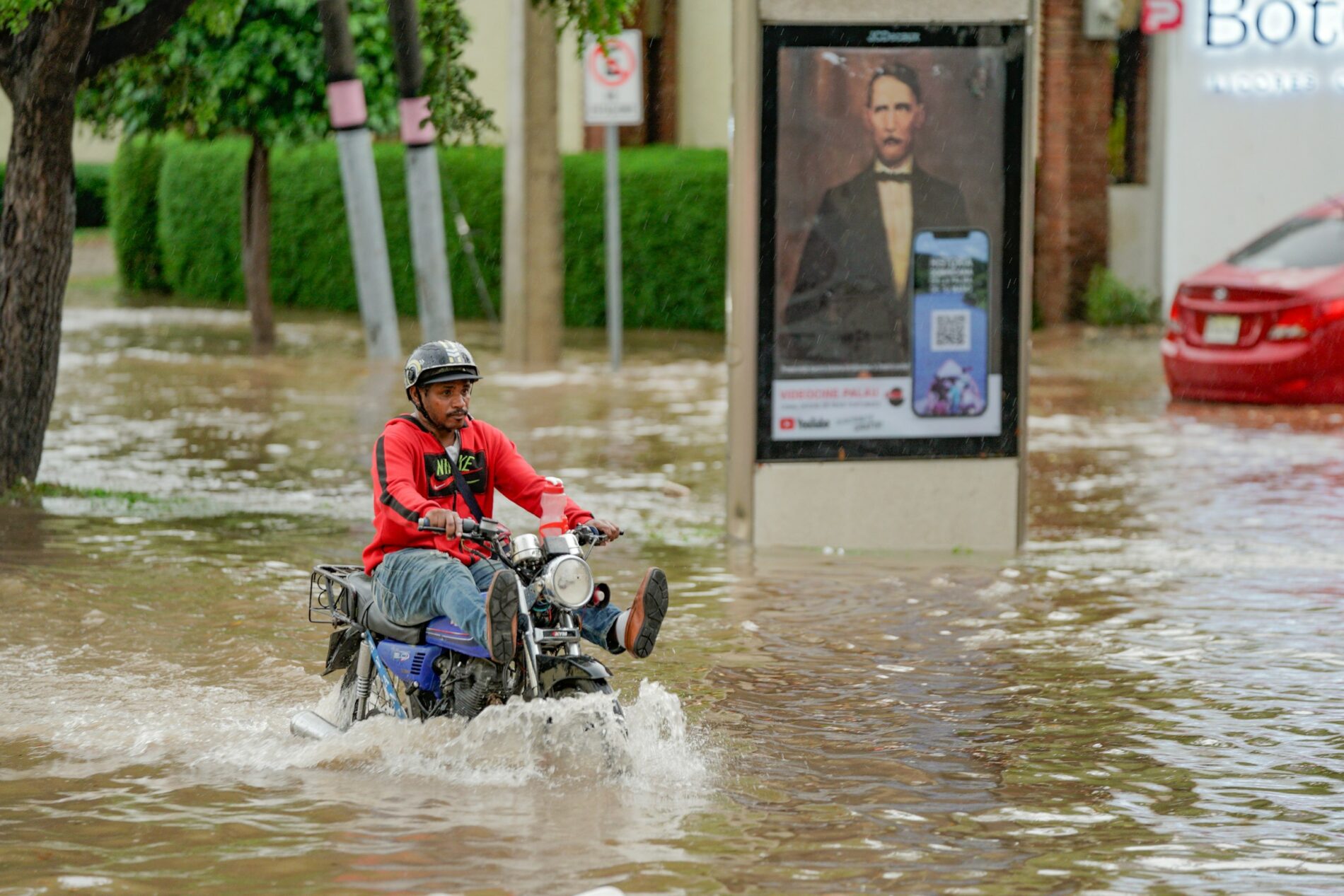 A man rides a motorbike through a flooded street.