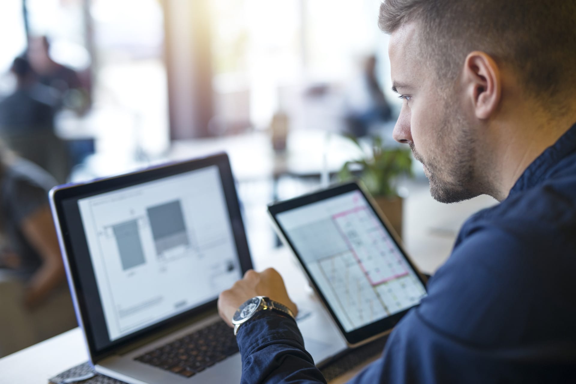 Team member of a logistics software development services company looking at his screen with a tablet in his right hand and typing with his left hand.