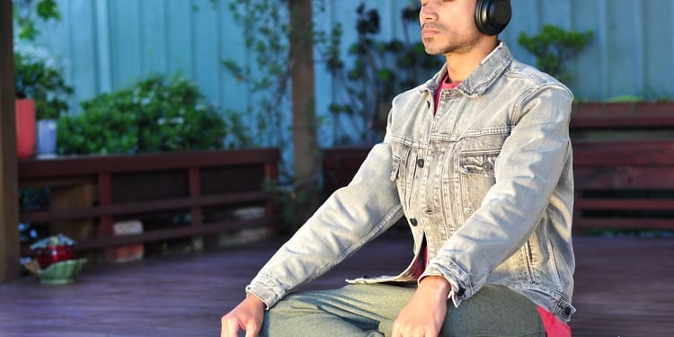 A man sitting on his yoga mat, managing stress through meditation.