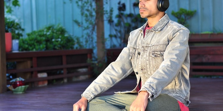 A man sitting on his yoga mat, managing stress through meditation.
